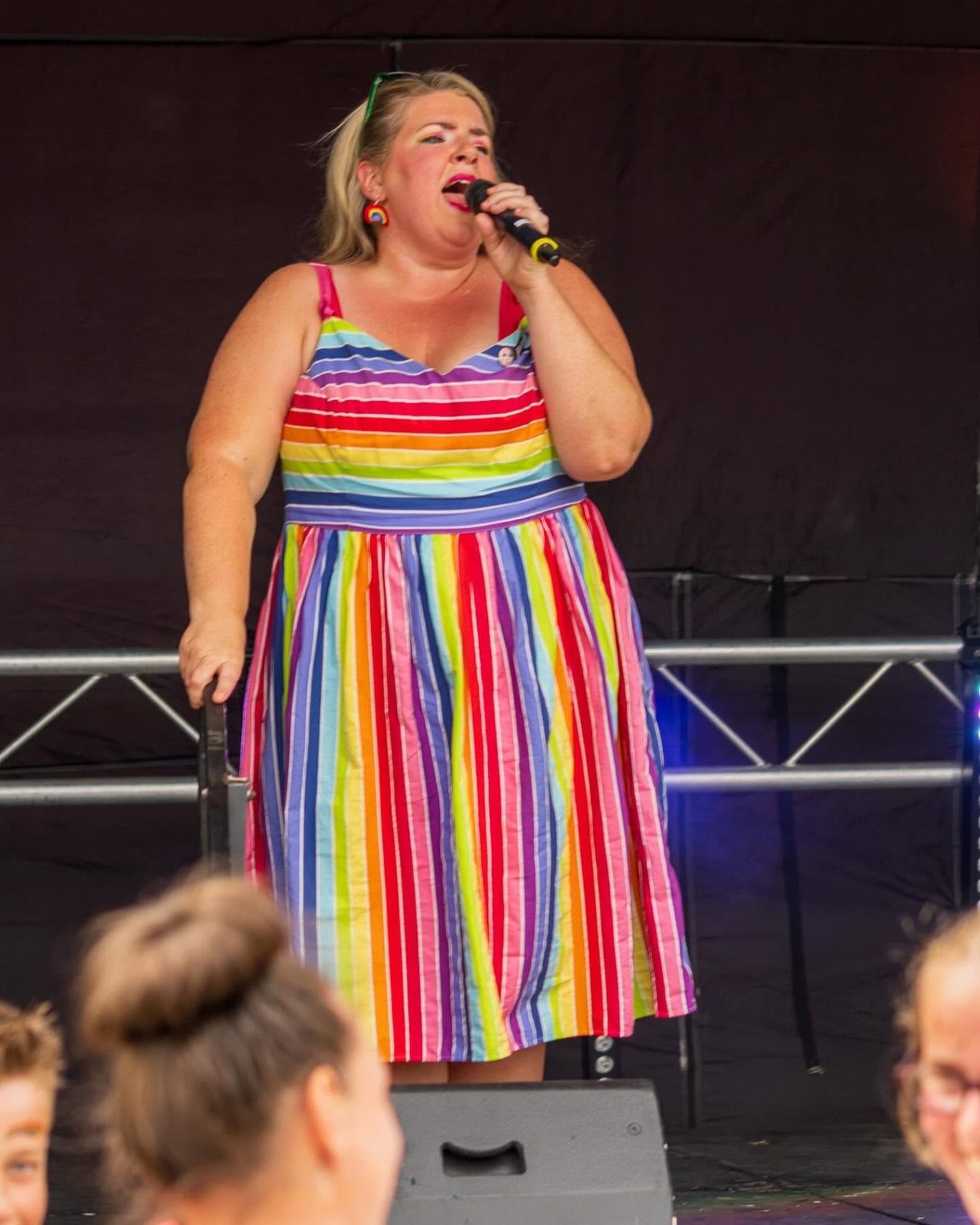 GYG - 2024 A performer in a rainbow-striped dress sings into a microphone on stage.
