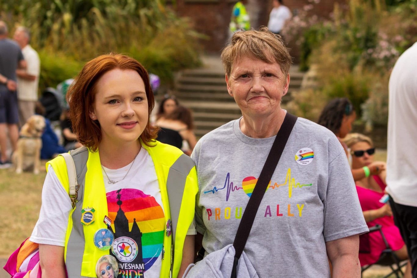 Two women smiling at a community event, one in a bright vest and the other in a T-shirt.