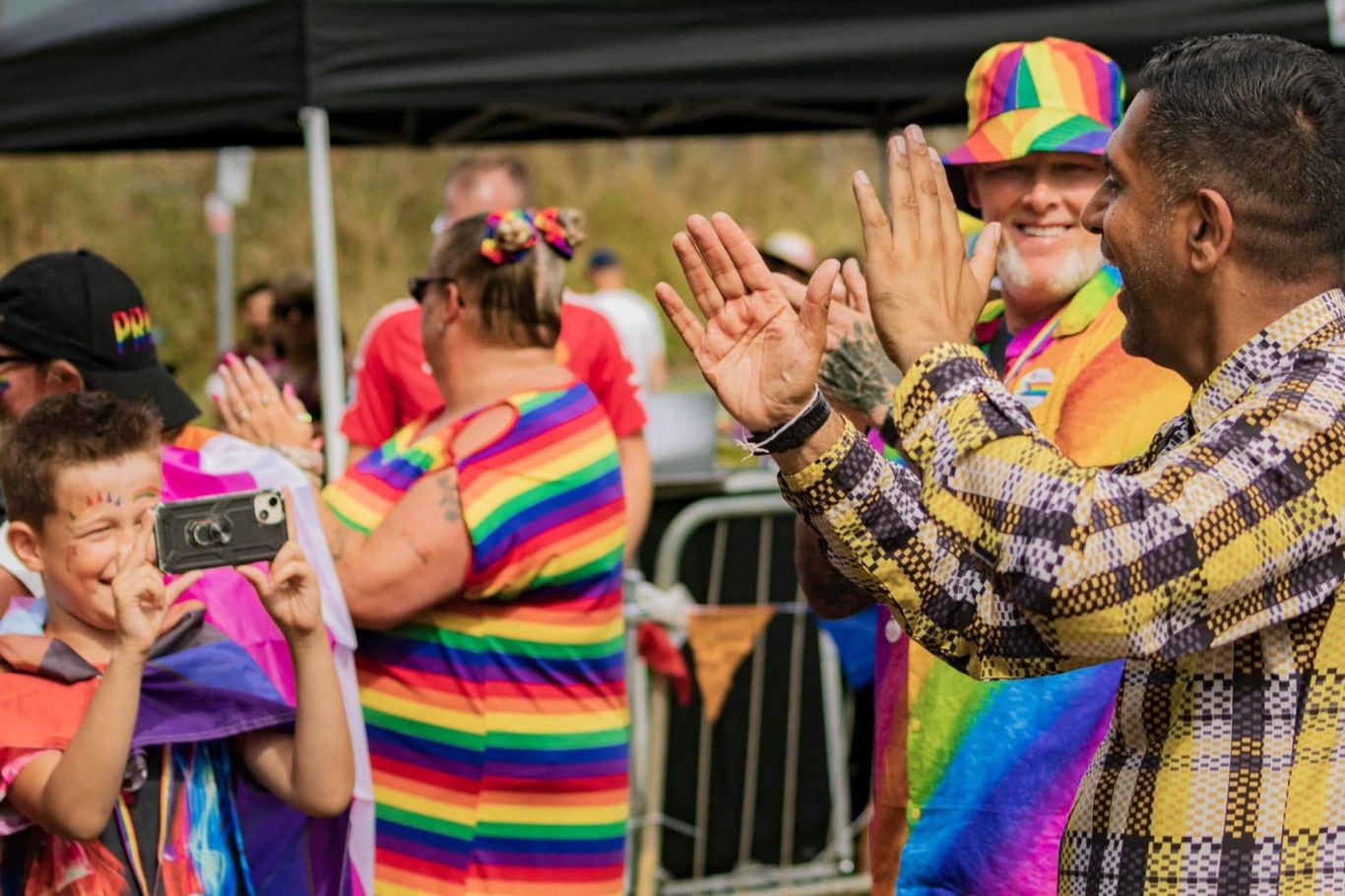 People celebrating at a vibrant pride event, wearing rainbow attire and smiling.