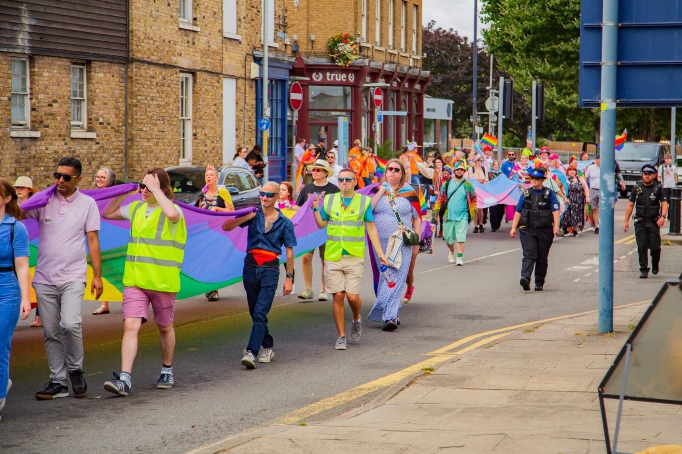 A vibrant parade with people holding rainbow flags and wearing colourful attire.