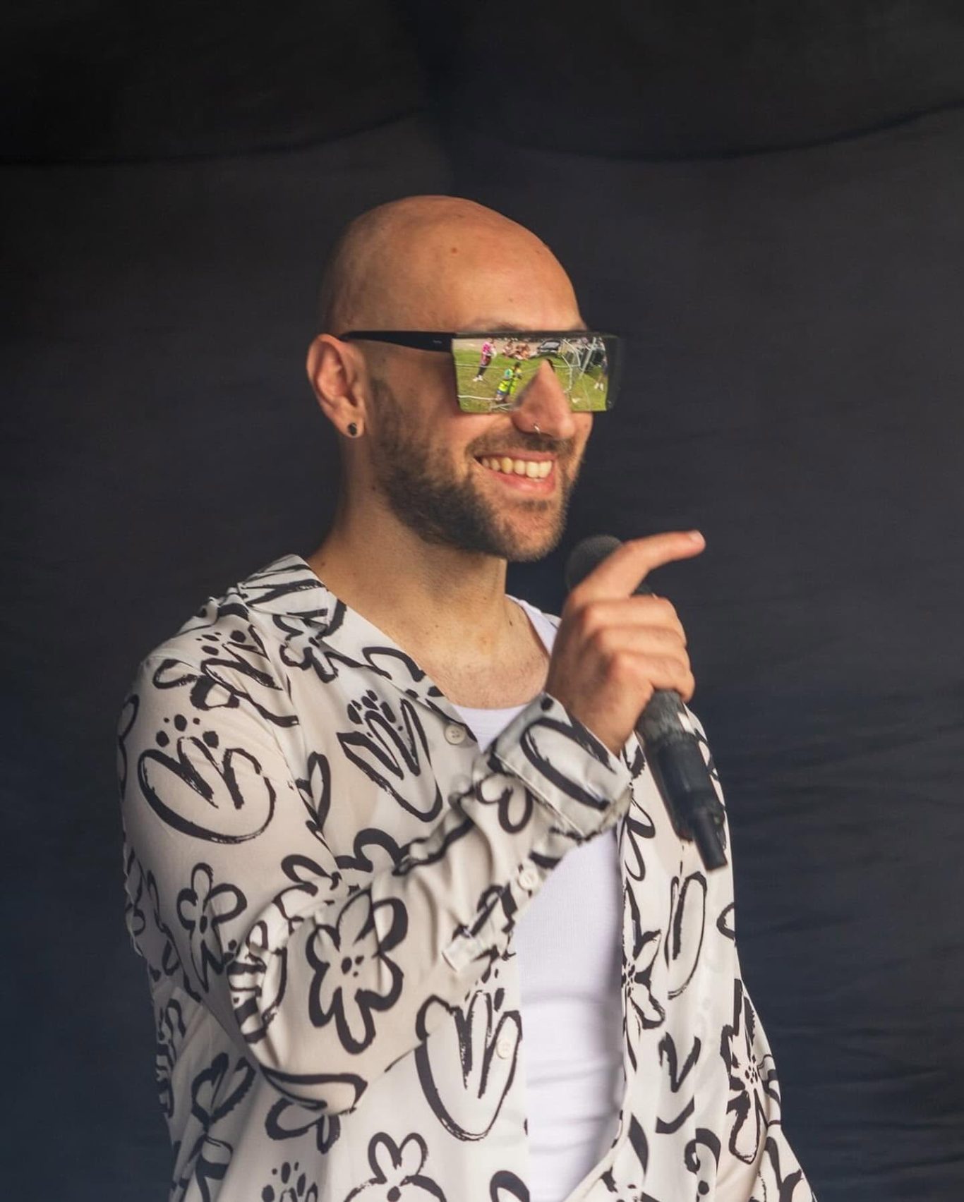 Neon Town - 2024 Smiling performer in patterned jacket and sunglasses, holding a microphone on stage.