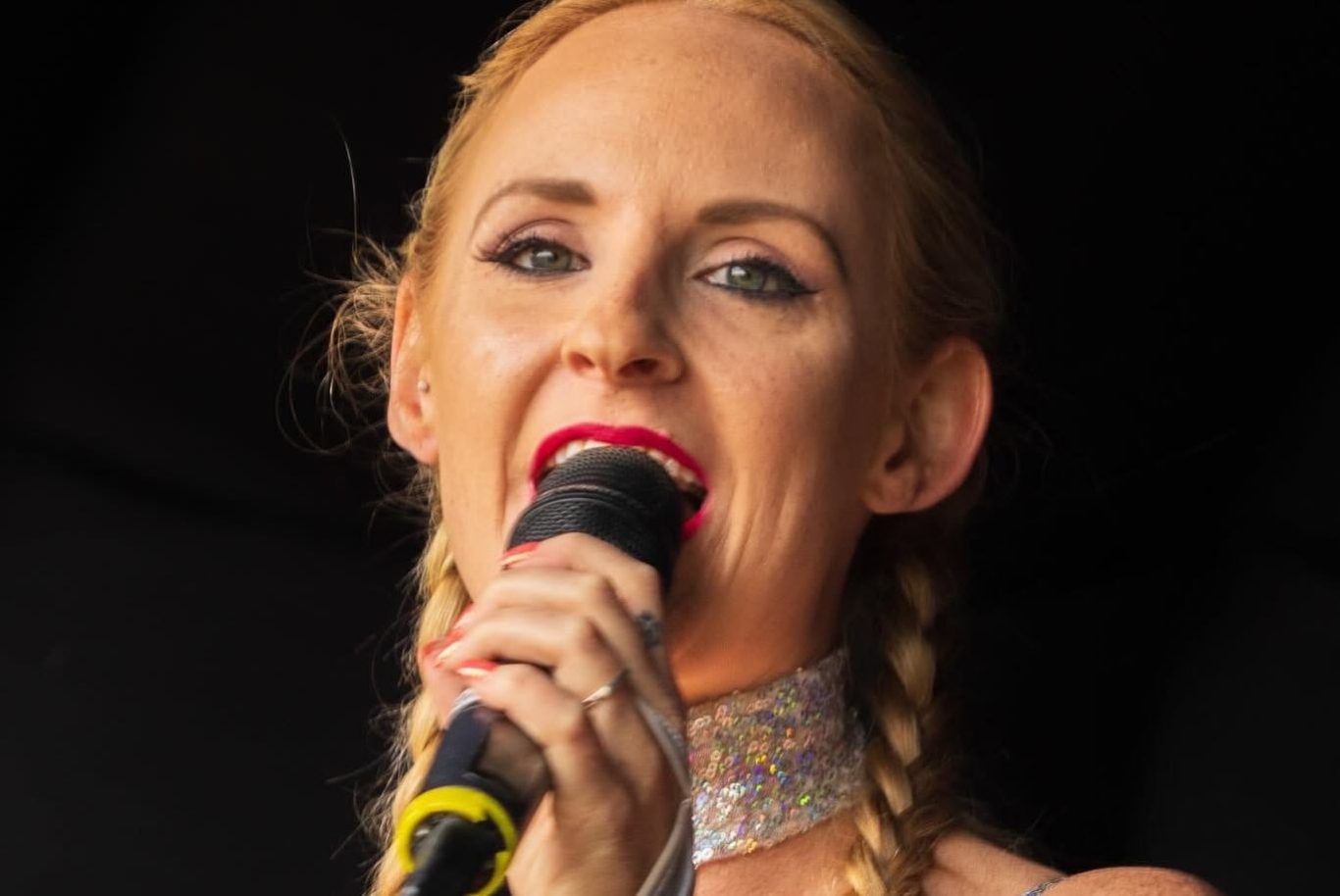 Kylie On Show - 2024 Woman singing into a microphone, wearing a sparkly outfit and red lipstick.