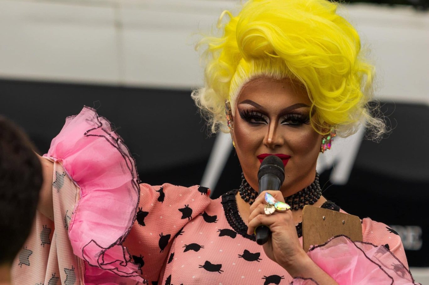 Amanda Bang - 2024 Drag performer with yellow hairstyle and pink outfit, speaking into a microphone.