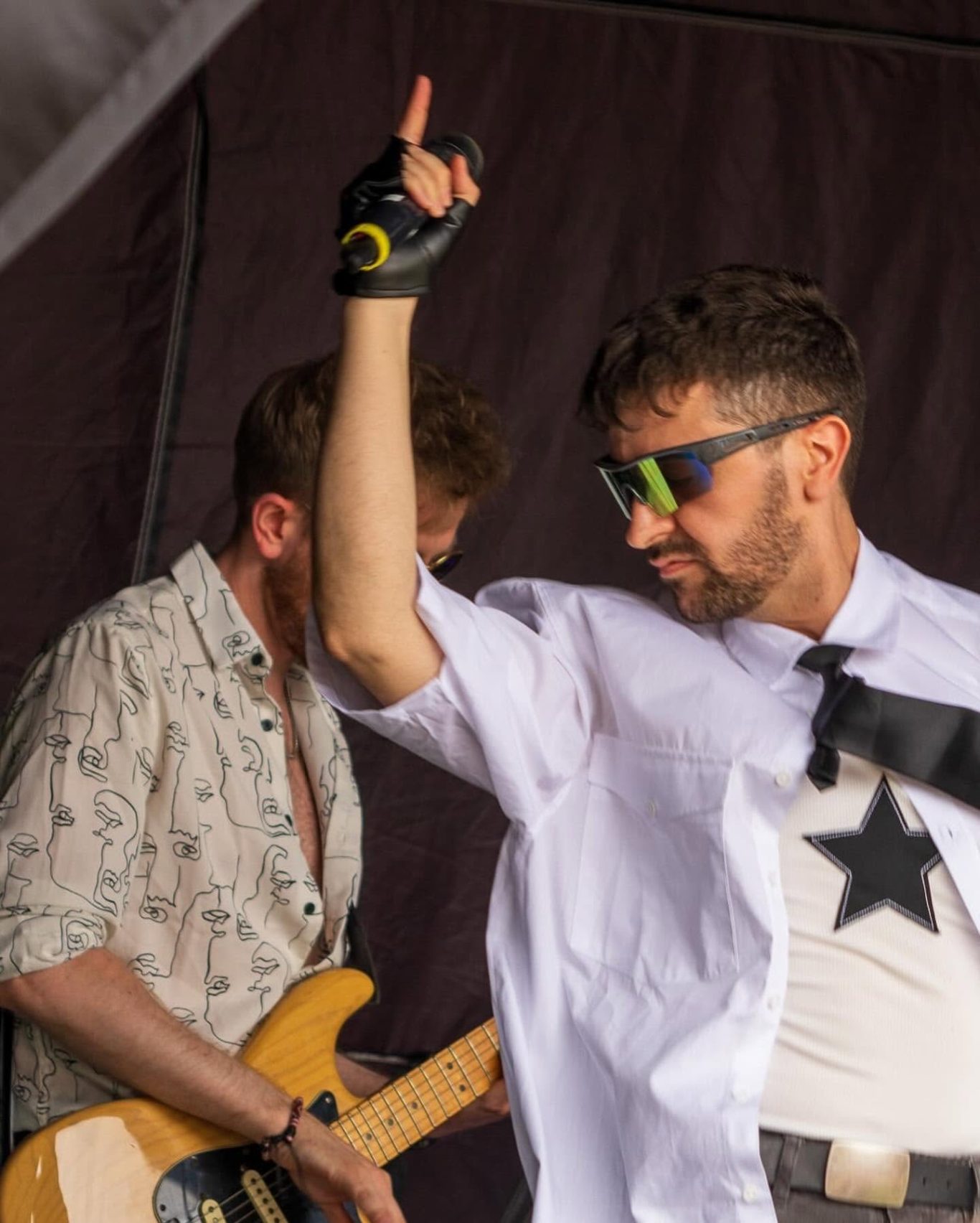 Neon Town - 2024 A performer in sunglasses gestures energetically on stage, with a guitarist in the background.