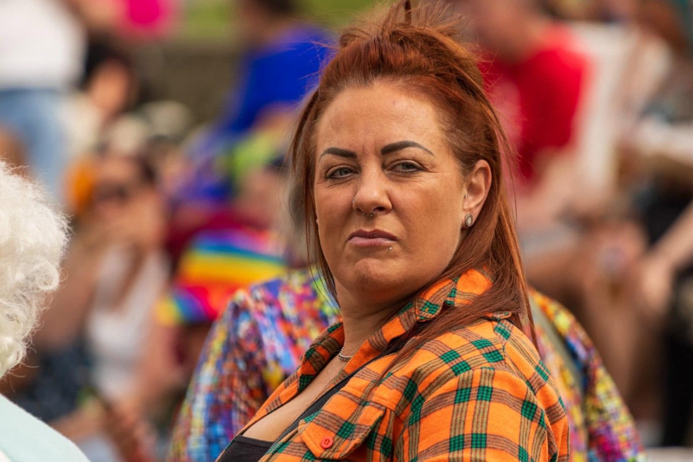 A woman with auburn hair and a checkered shirt looking intently at the camera.