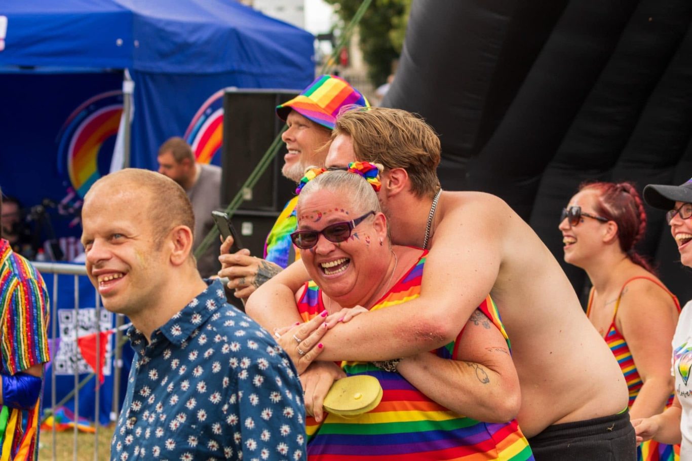 A joyful crowd at a pride event, featuring people in vibrant rainbow clothing and celebrations.