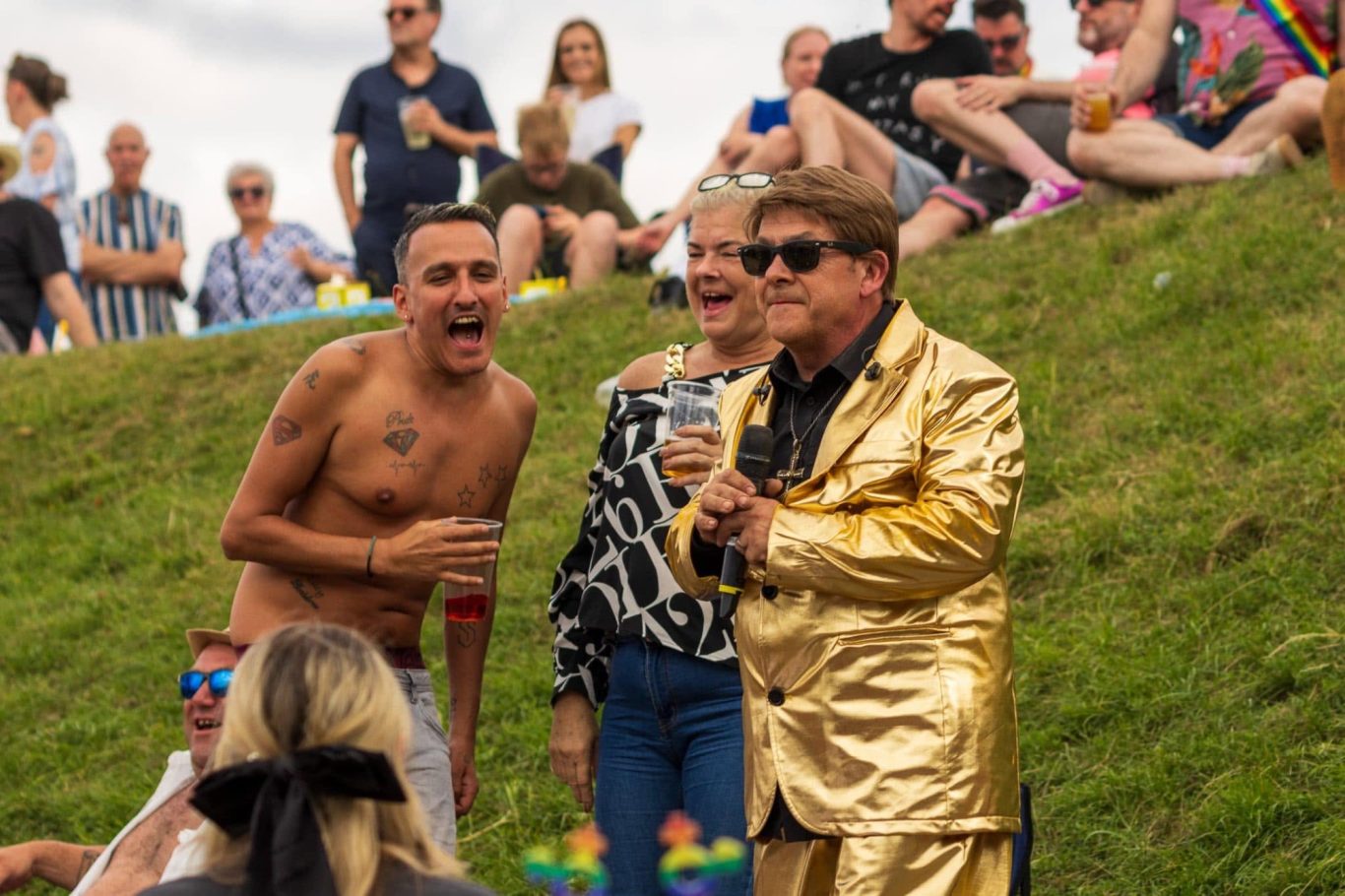 Elton John Tribute A lively gathering with people enjoying a celebration on a grassy hillside.