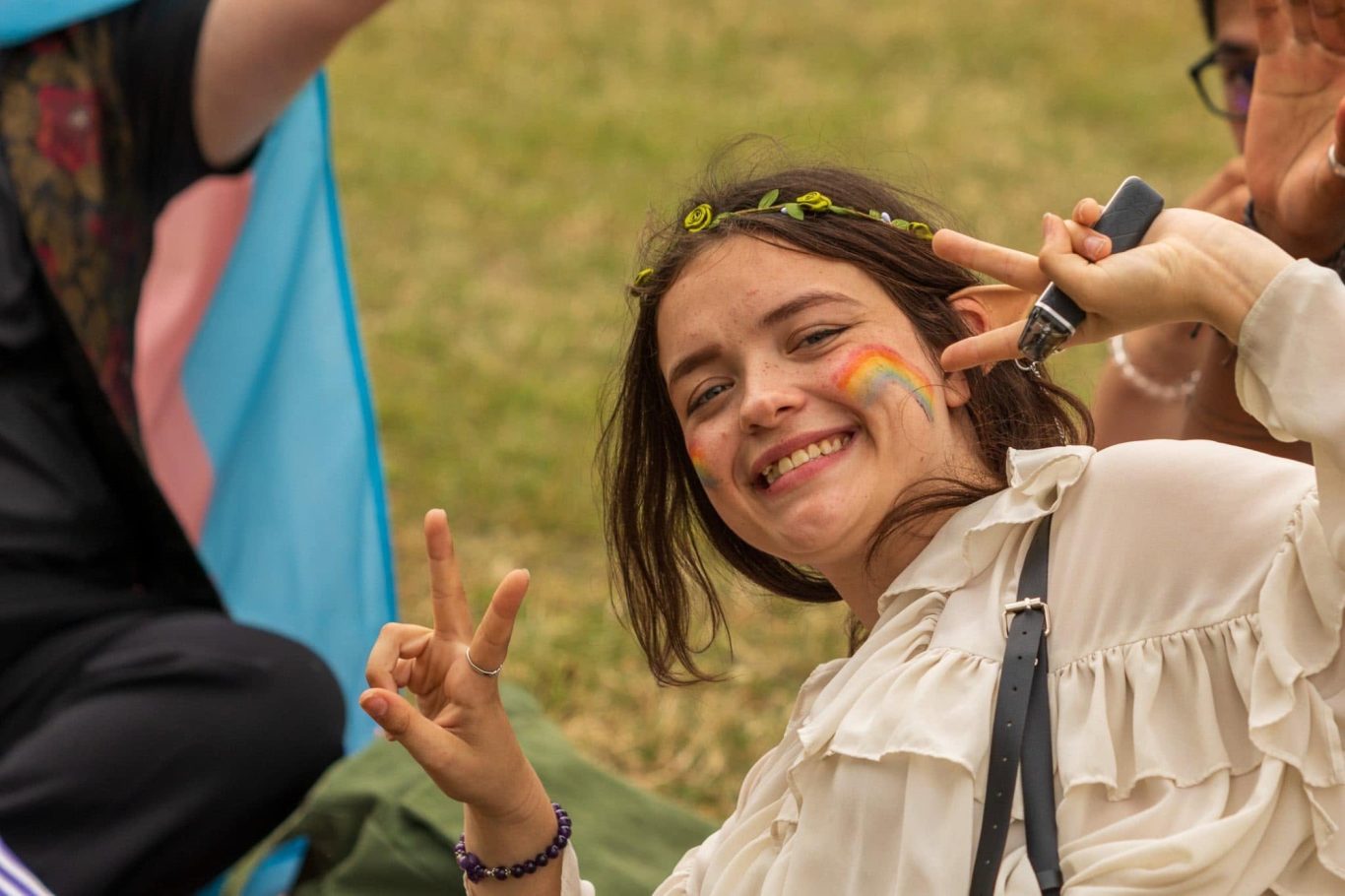 Young woman smiling and making a peace sign, with face paint and flowers in her hair.