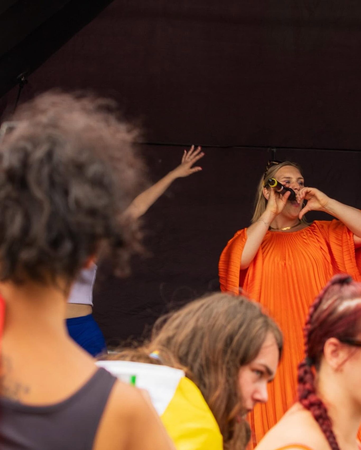 GYG - 2024 A performer in an orange outfit poses on stage while an audience member watches.