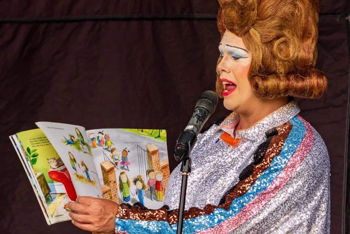 Mama G - 2024 A performer in a sparkling outfit narrates from a colourful storybook.