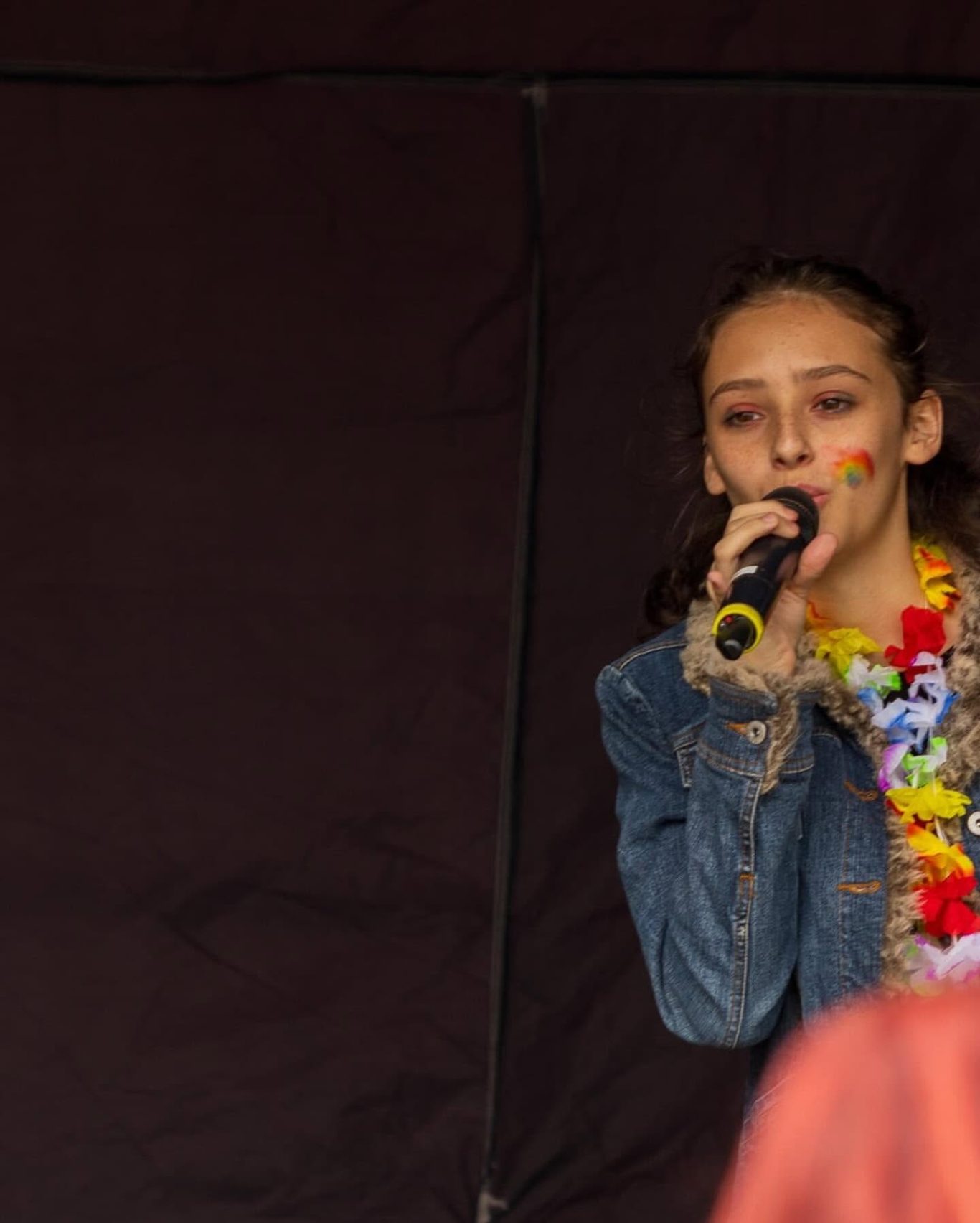 GYG - 2024 Young girl singing into a microphone, wearing a floral necklace and denim jacket.