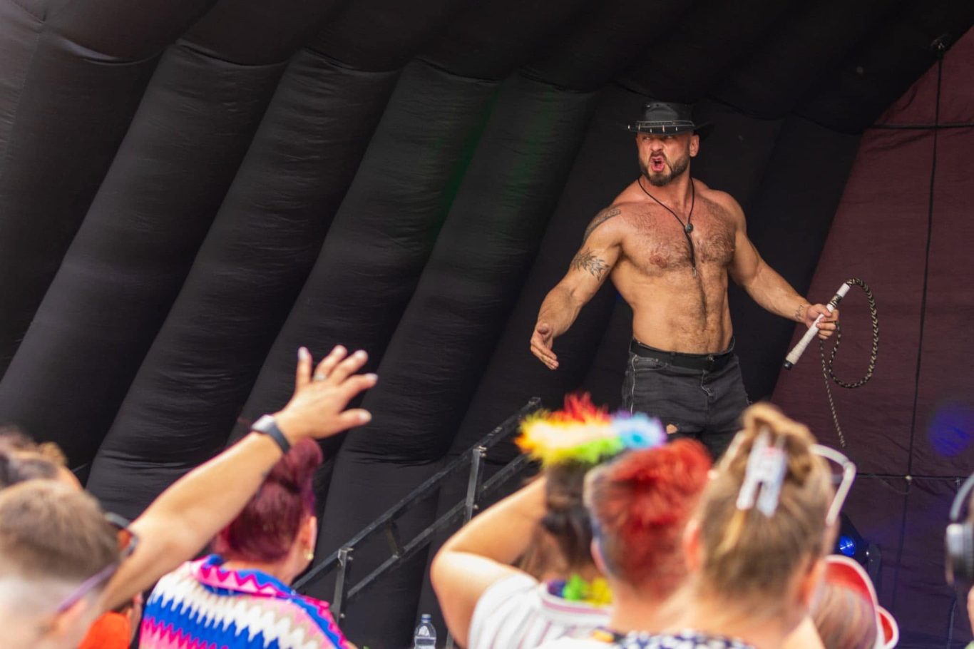 Marshall Arkley - 2024 A shirtless performer with a hat engaging with an audience at a lively event.