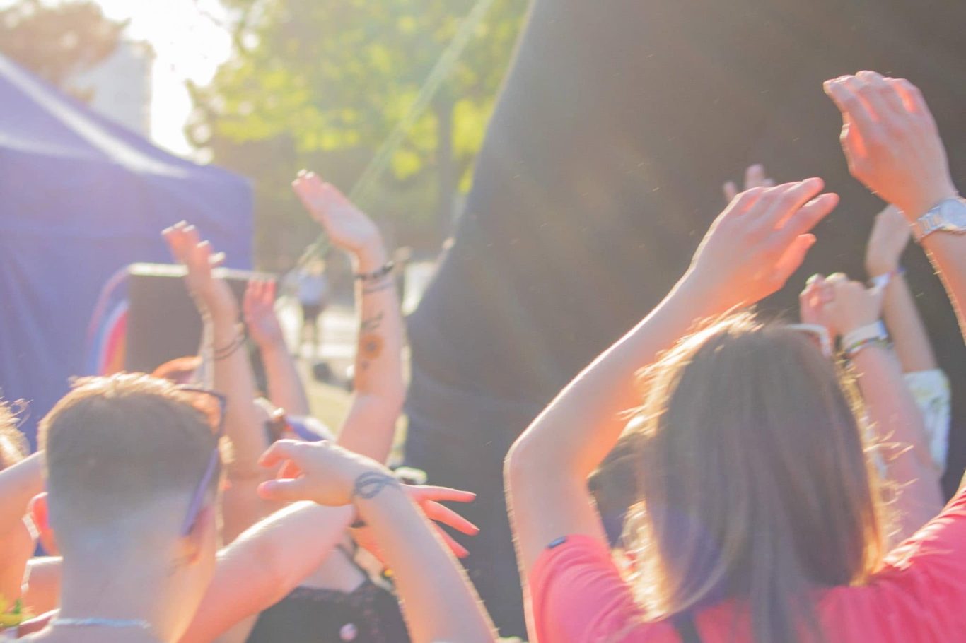 Crowd with raised hands enjoying an outdoor event in bright sunlight.