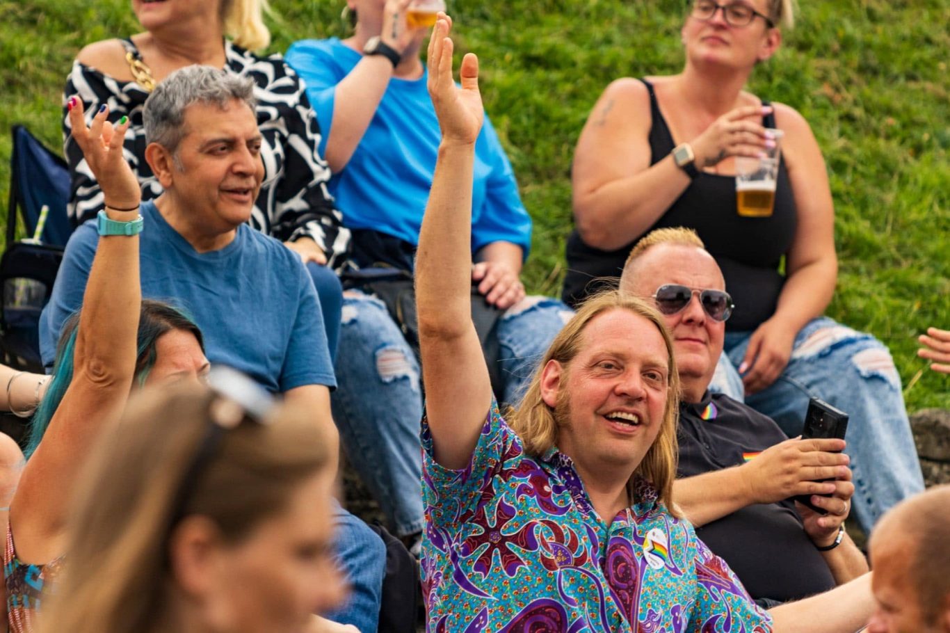 Crowd of people at an outdoor event, some raising hands and holding drinks.