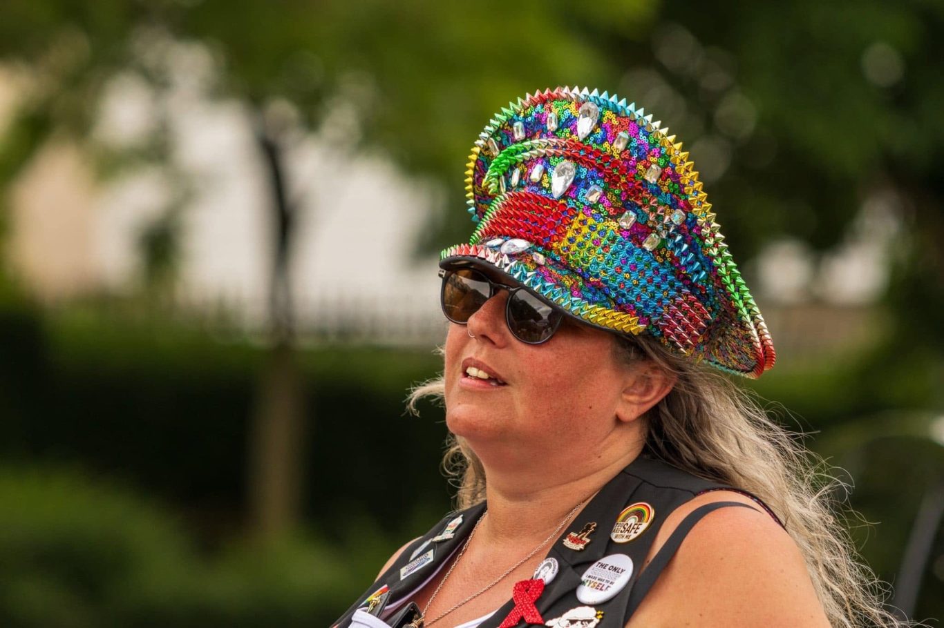 Woman with long hair wearing a colourful hat and sunglasses, smiling at an outdoor event.