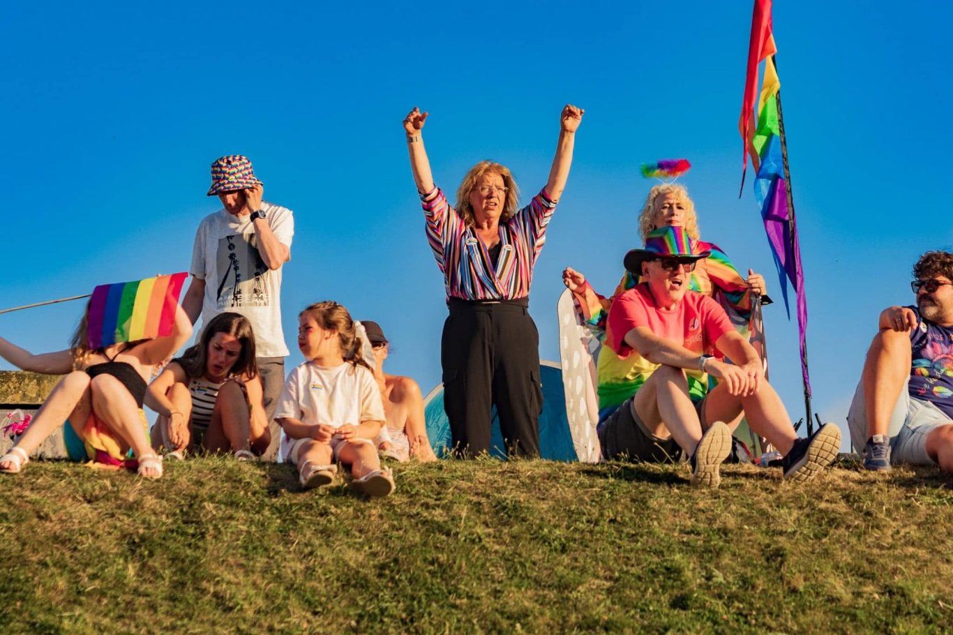 Group of people celebrating outdoors with rainbow flags and vibrant attire.
