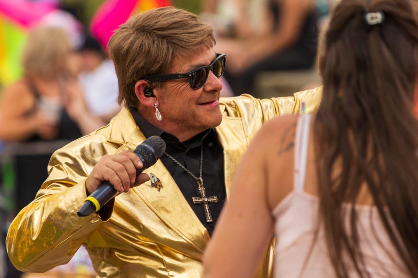 Elton John Tribute Man in a gold jacket singing with a microphone at an outdoor event.