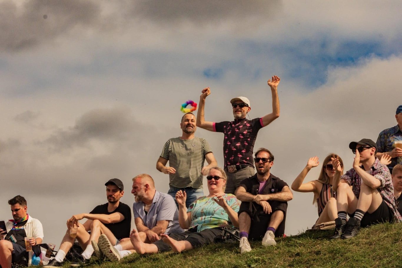 A diverse group of people sitting on a hillside, waving and celebrating joyfully.