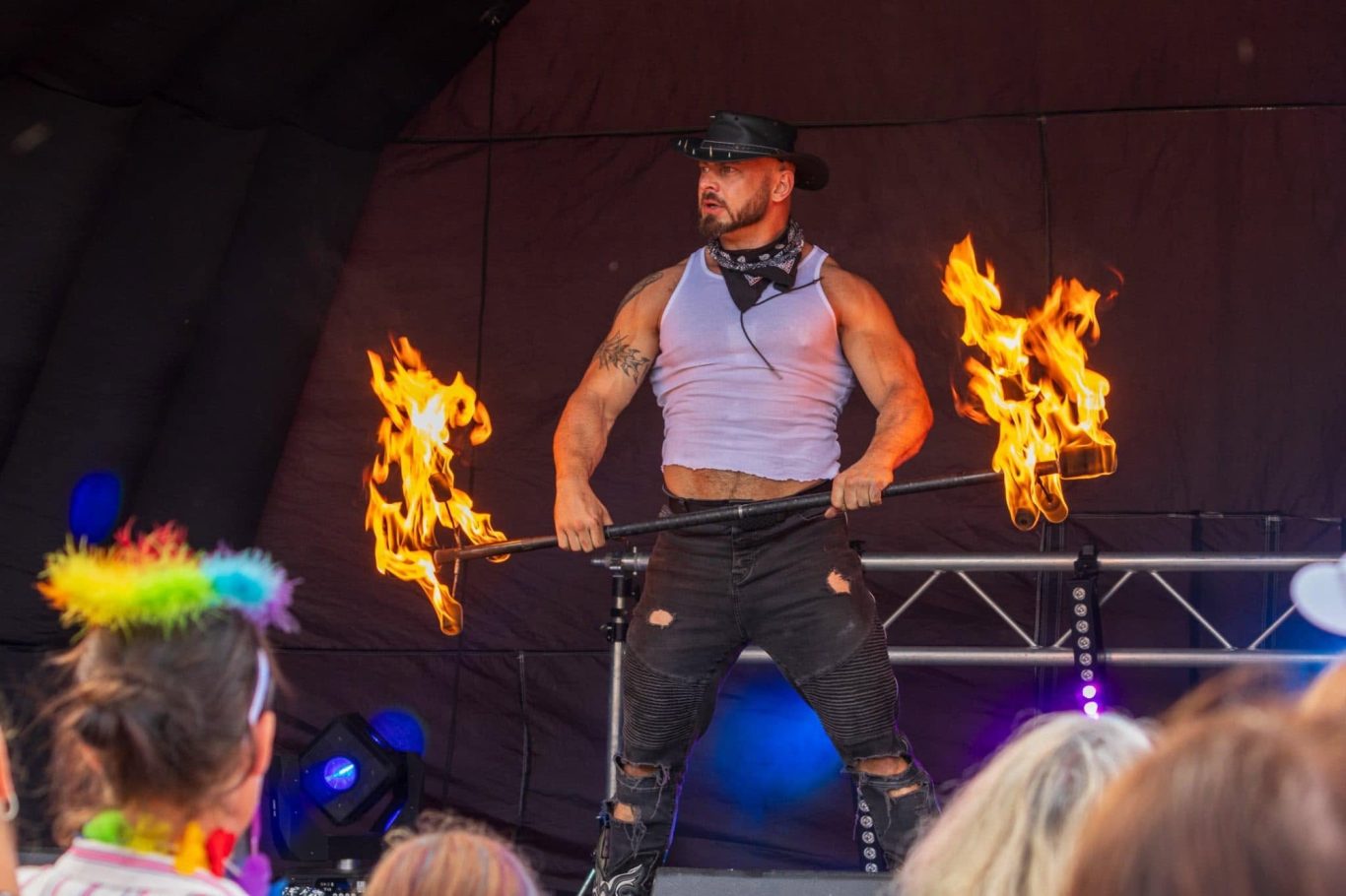 Marshall Arkley - 2024 Fire performer in a sleeveless shirt entertains the crowd with flaming sticks.