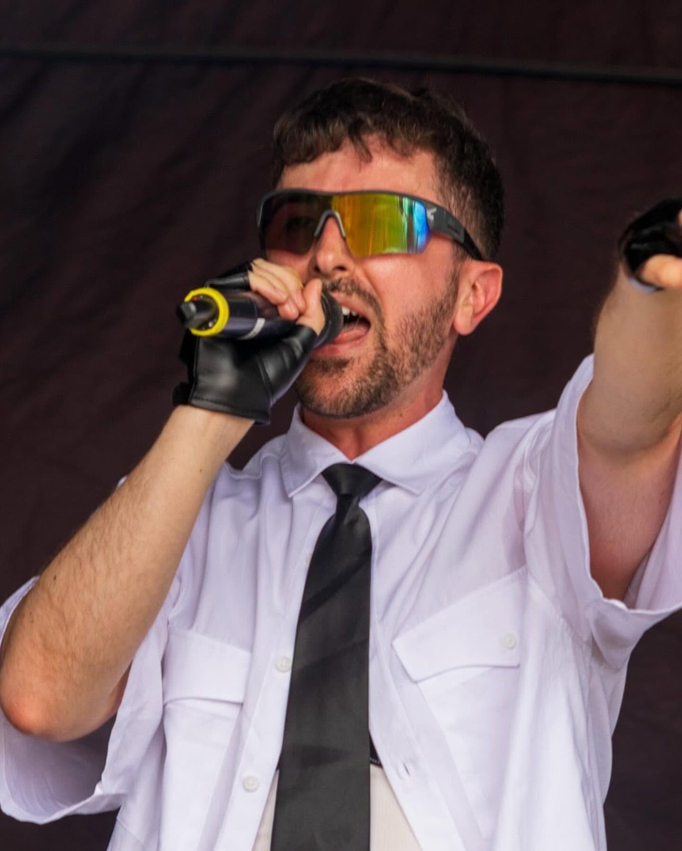 Neon Town - 2024 A singer in a white shirt and tie, wearing sunglasses, passionately performing on stage.
