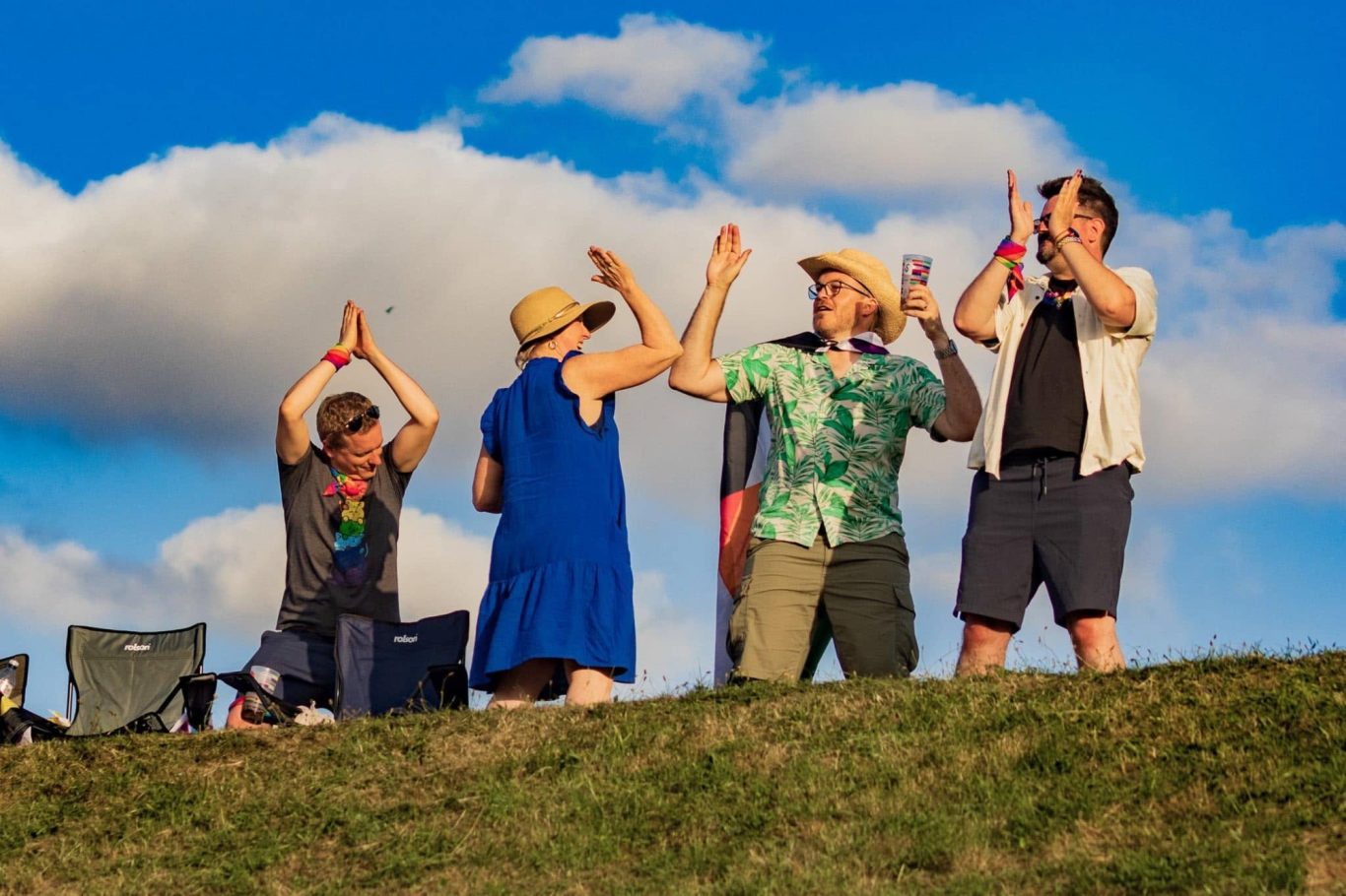 People celebrating on a hill, clapping and enjoying the outdoors under a blue sky.