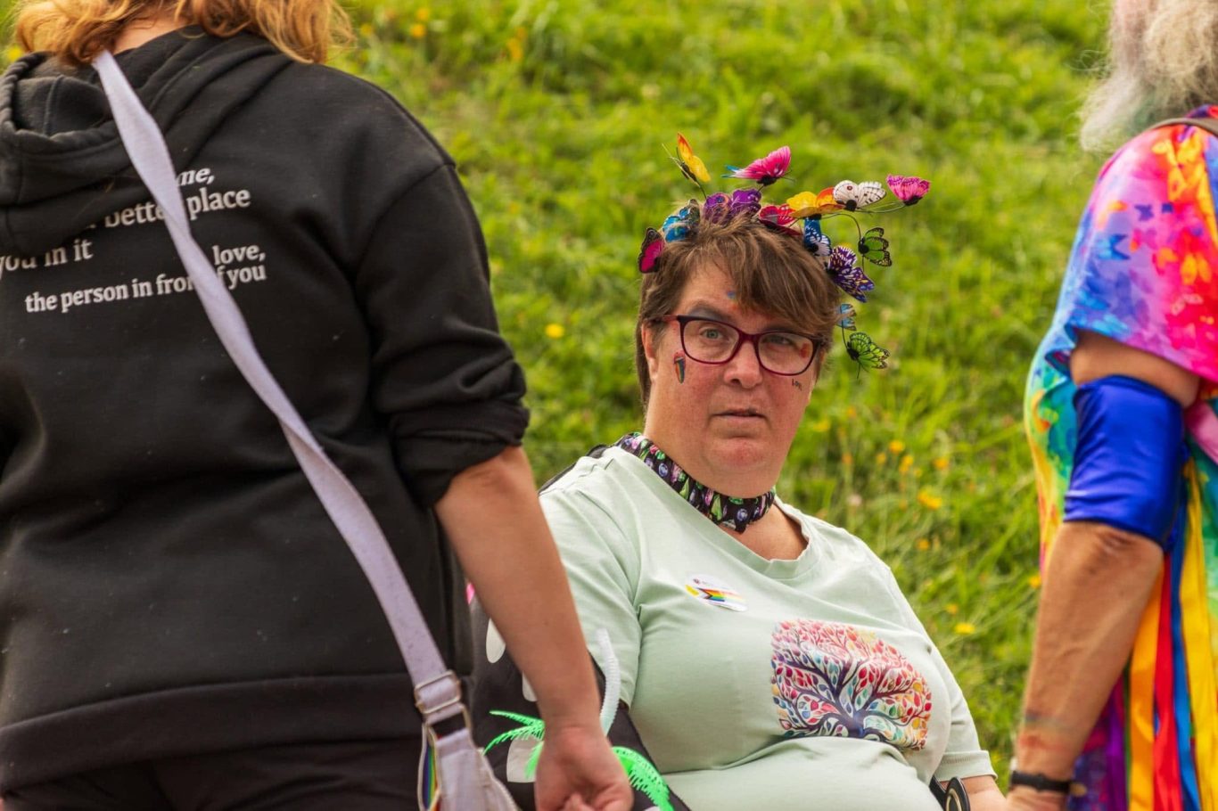 A woman with glasses and a colourful headband looks curiously at someone nearby.
