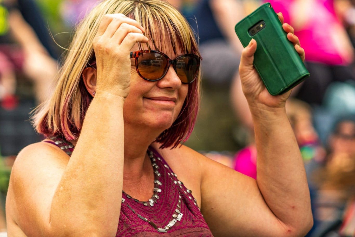 Smiling woman with sunglasses holding a phone, wearing a casual outfit.