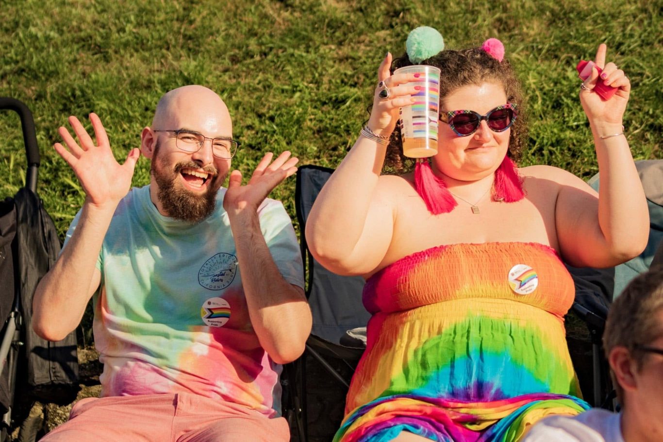 Two cheerful people at a rainbow-themed event, enjoying refreshments and celebrating.
