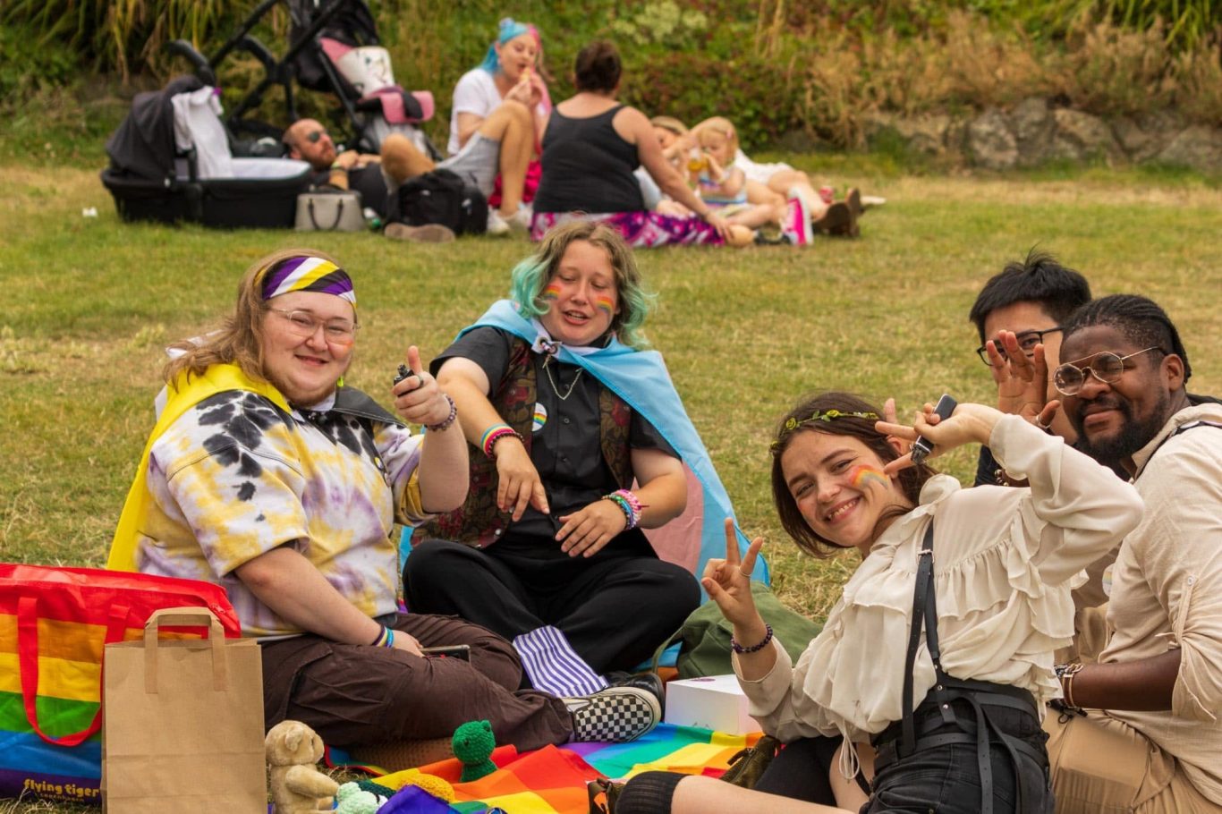 Group of five people smiling and posing on a picnic blanket at an outdoor event.