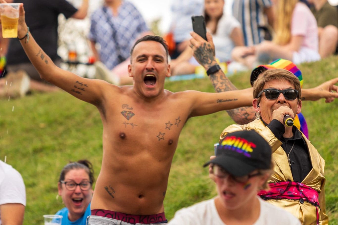 Cheerful group celebrating at an outdoor event, wearing rainbow accessories and enjoying drinks.