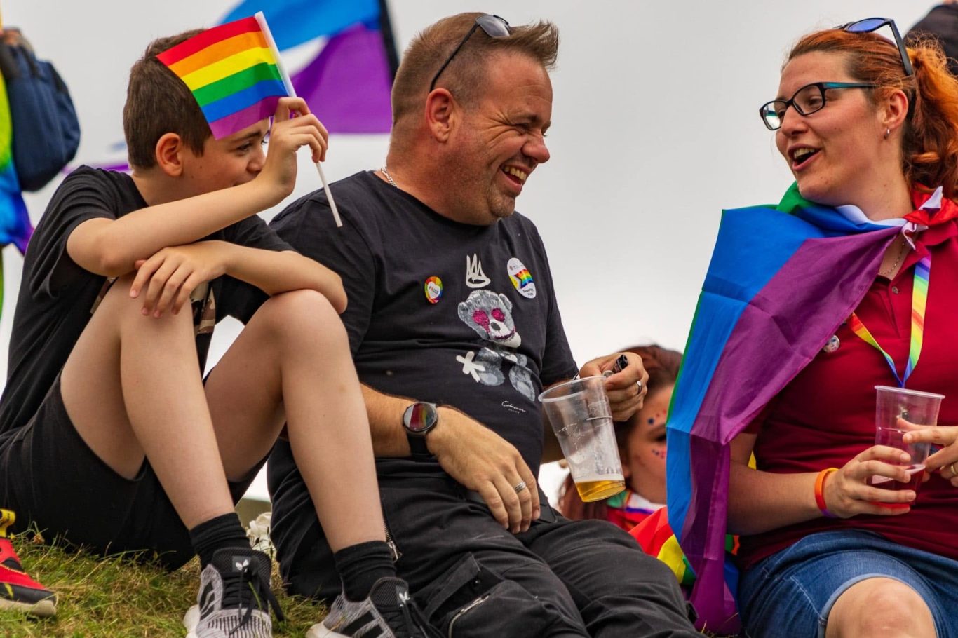 A group of people at a pride event, holding flags and enjoying drinks.