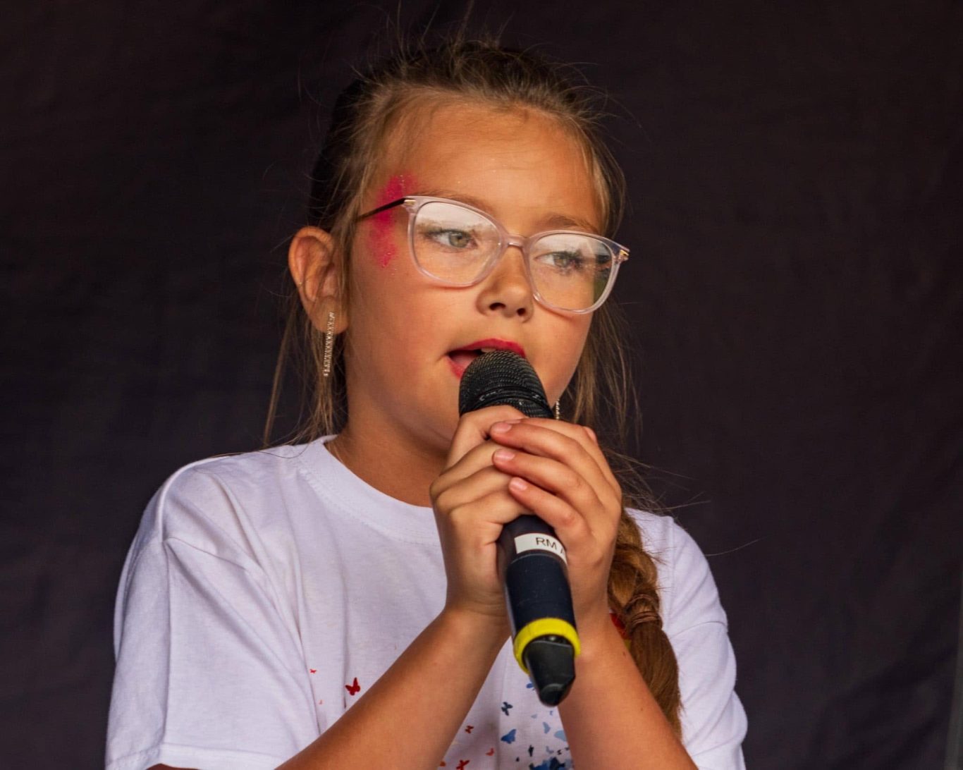 GYG - 2024 A young girl with glasses sings into a microphone at a performance.