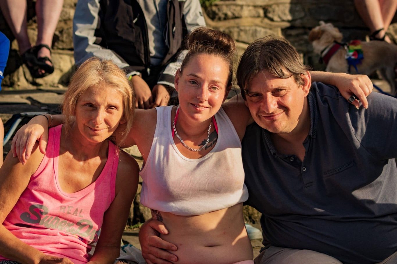 Three people smiling together, seated outdoors in casual clothing.