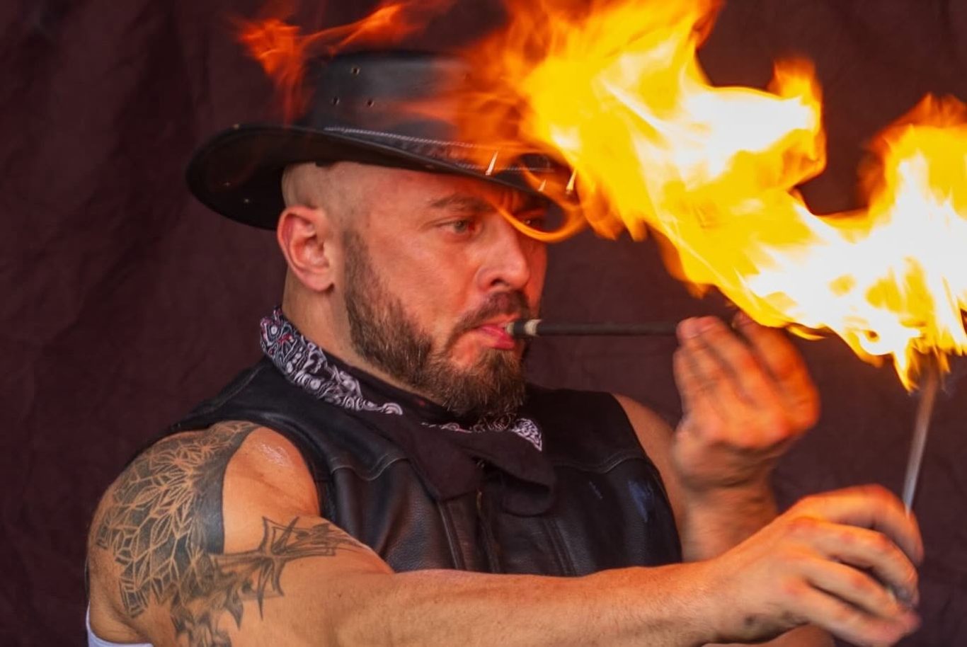 Marshall Arkley - 2024 Fire performer with a hat, creating flames from a stick in a dramatic display.
