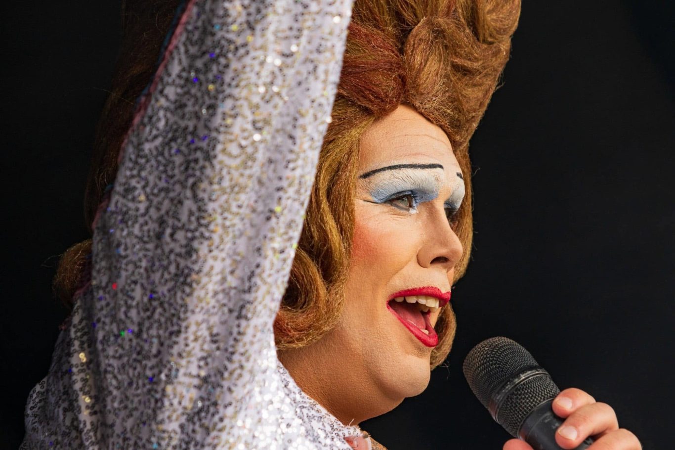 Mama G - 2024 A performer with elaborate makeup and a stylish hairdo sings into a microphone.