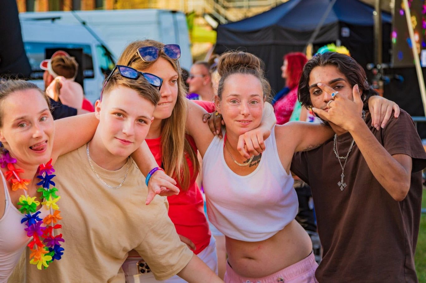 A group of five young adults smiling and posing together at a lively outdoor event.