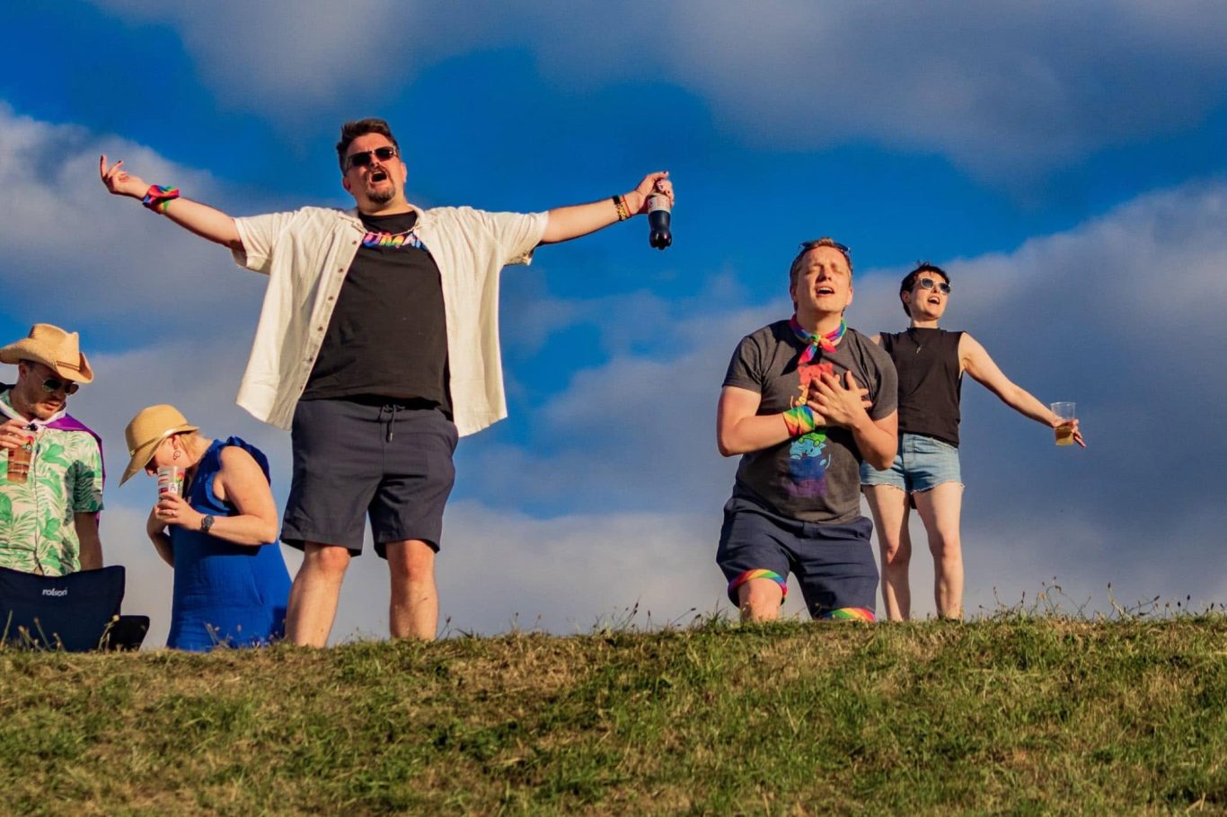 A group of people celebrating outdoors with raised arms against a cloudy sky.