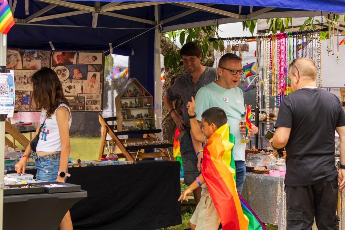 A vibrant market stall at a pride event with rainbow decorations and diverse visitors.