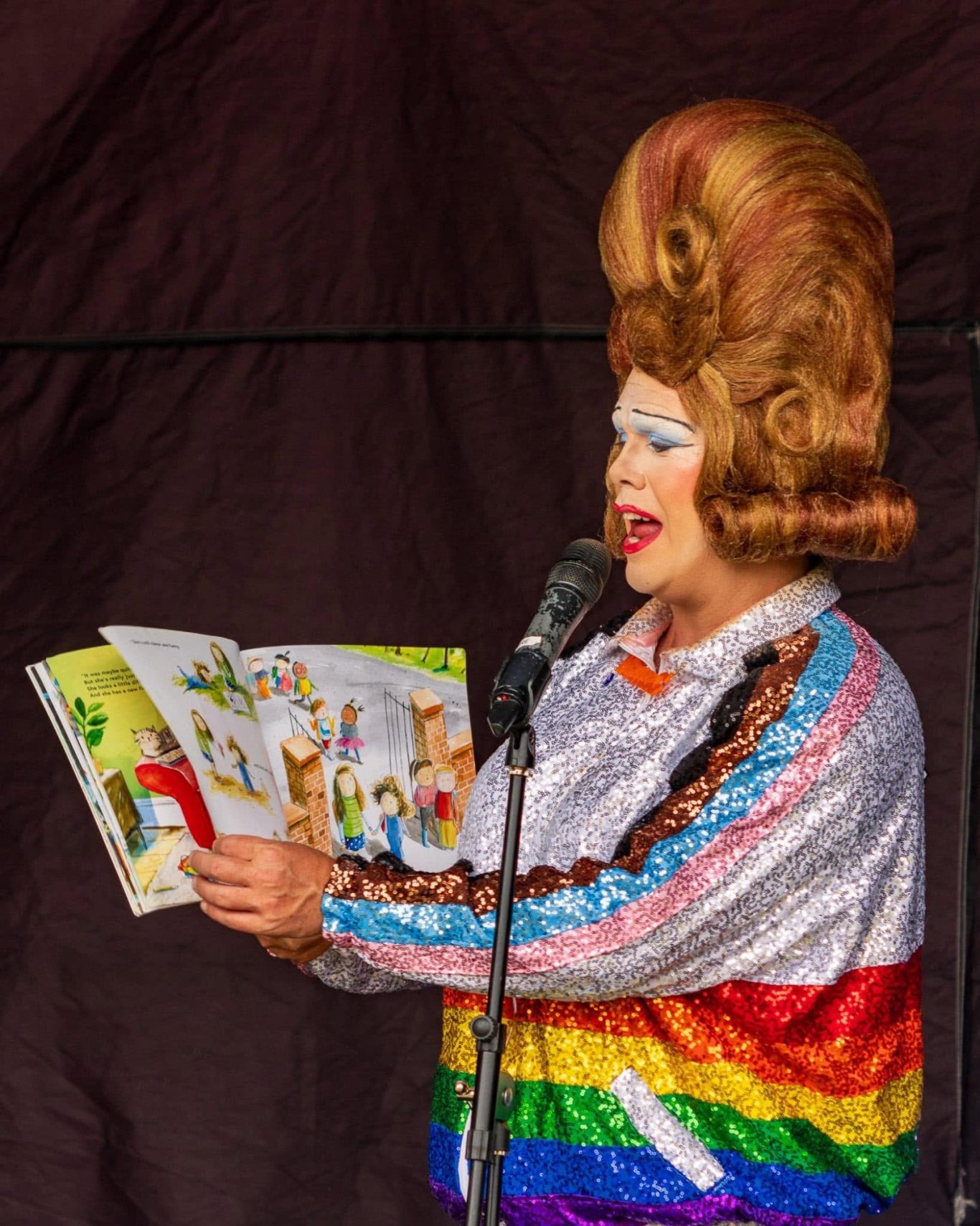Mama G - 2024 A performer in a colourful outfit reads from a children's book.