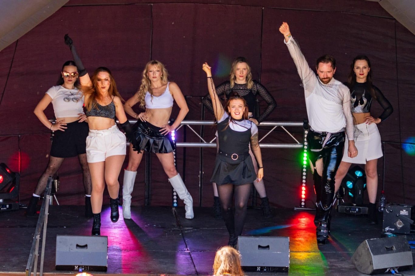 Haus of Heels - 2024 A group of six performers in stylish outfits dancing on stage with colourful lights.