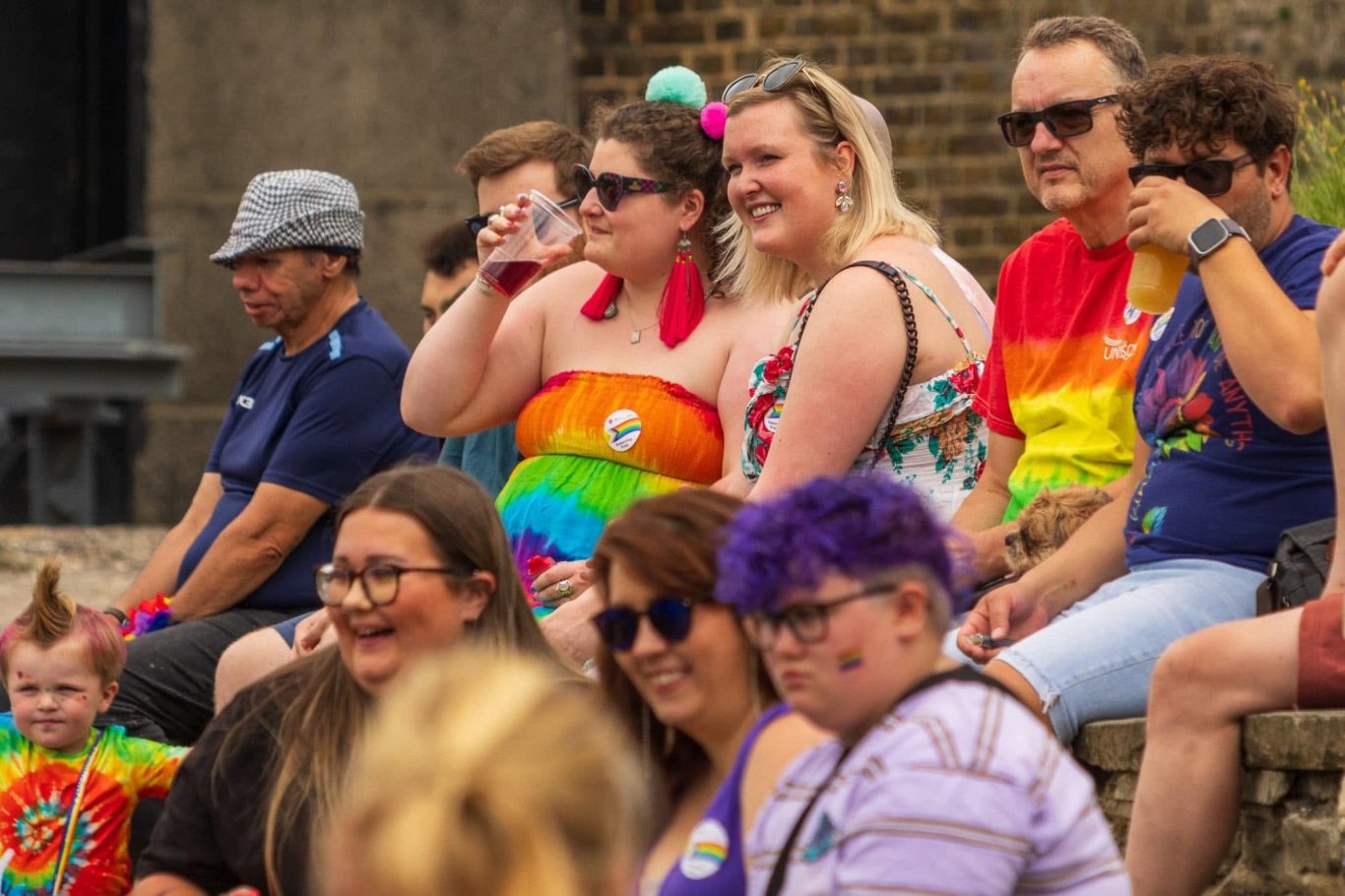 Diverse group of people smiling and enjoying a festive outdoor event, some in vibrant outfits.