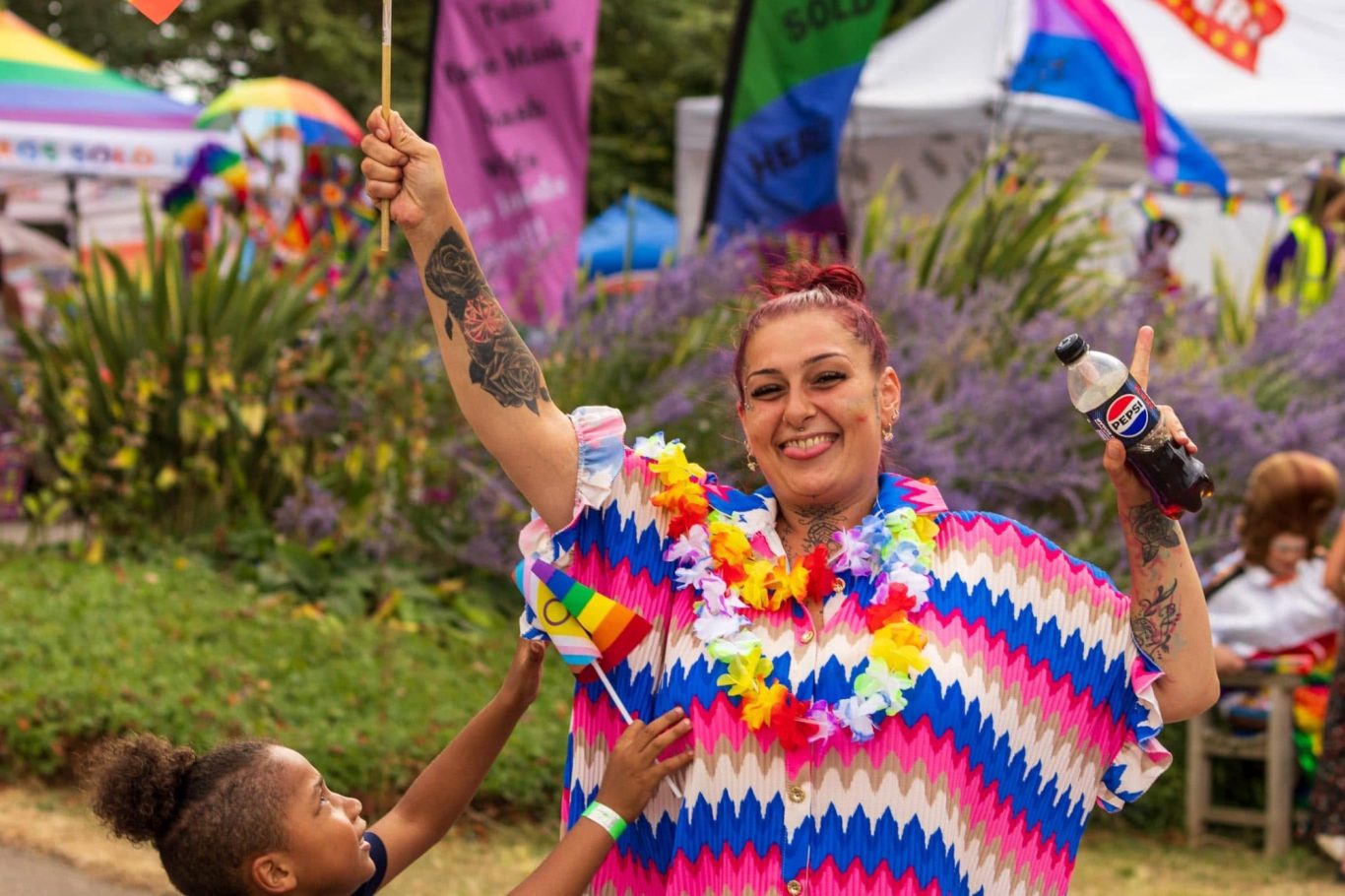 Woman in a colourful outfit celebrates at an outdoor festival with a child.
