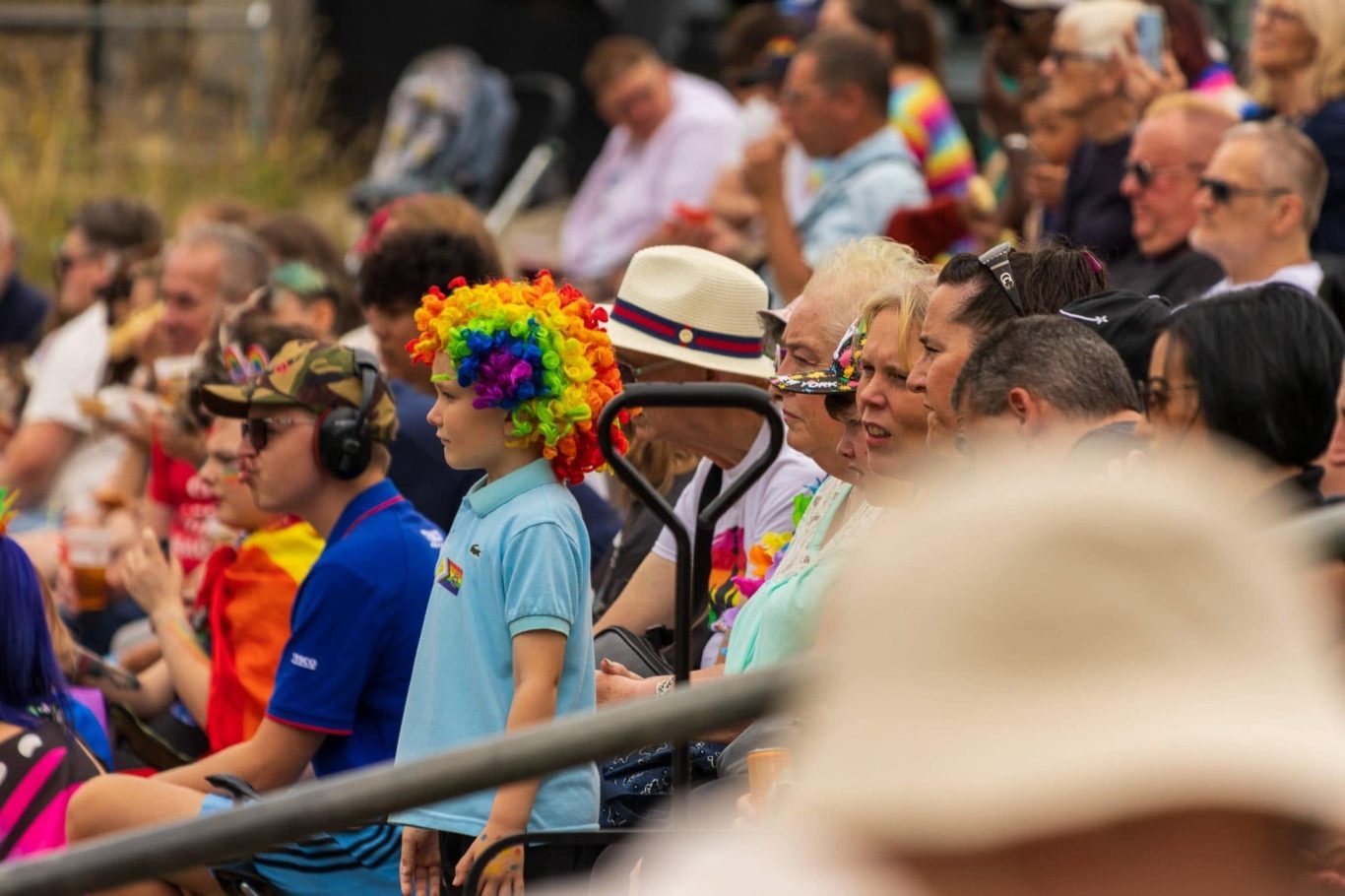 Crowd at an event, featuring colourful outfits and a person in a hat with a rainbow wig.