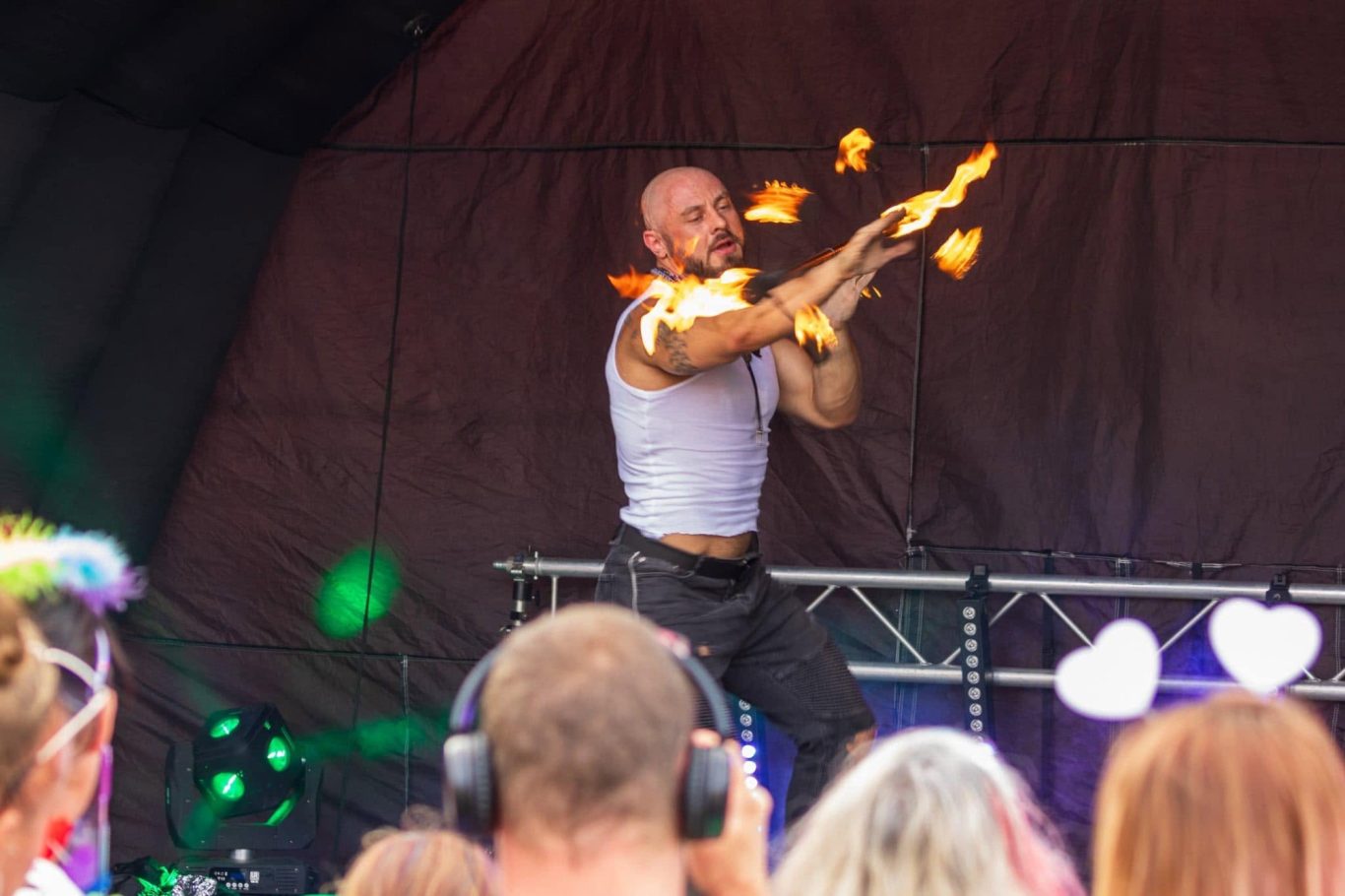 Marshall Arkley - 2024 A performer juggling flaming torches on stage during an outdoor event.