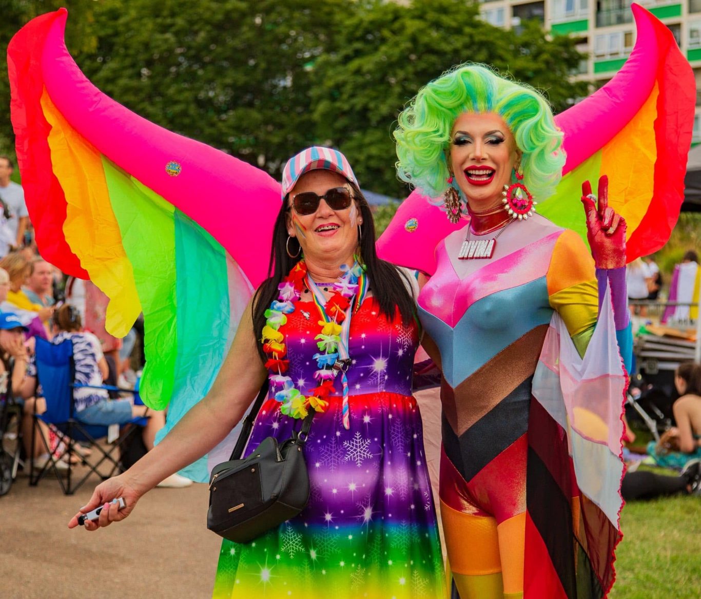 Two individuals stand together, one in vibrant, multicoloured wings and the other in a rainbow dress.