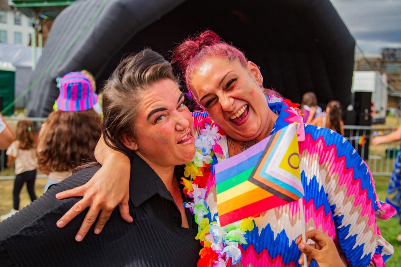 Two women smiling and posing joyfully, wearing colourful outfits at an outdoor event.