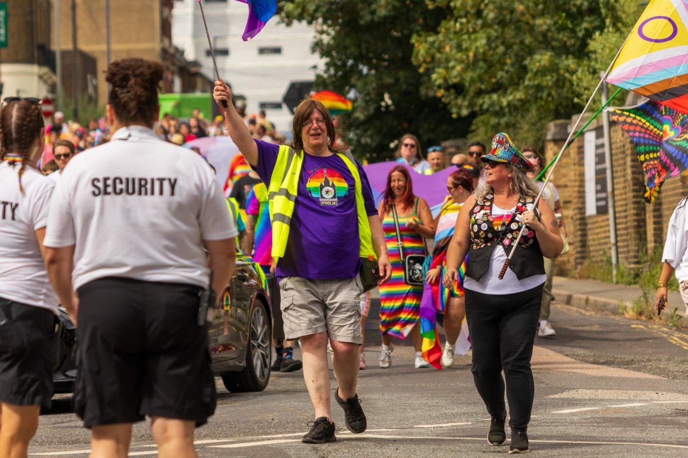 People celebrating at a pride parade, wearing vibrant clothing and waving flags.
