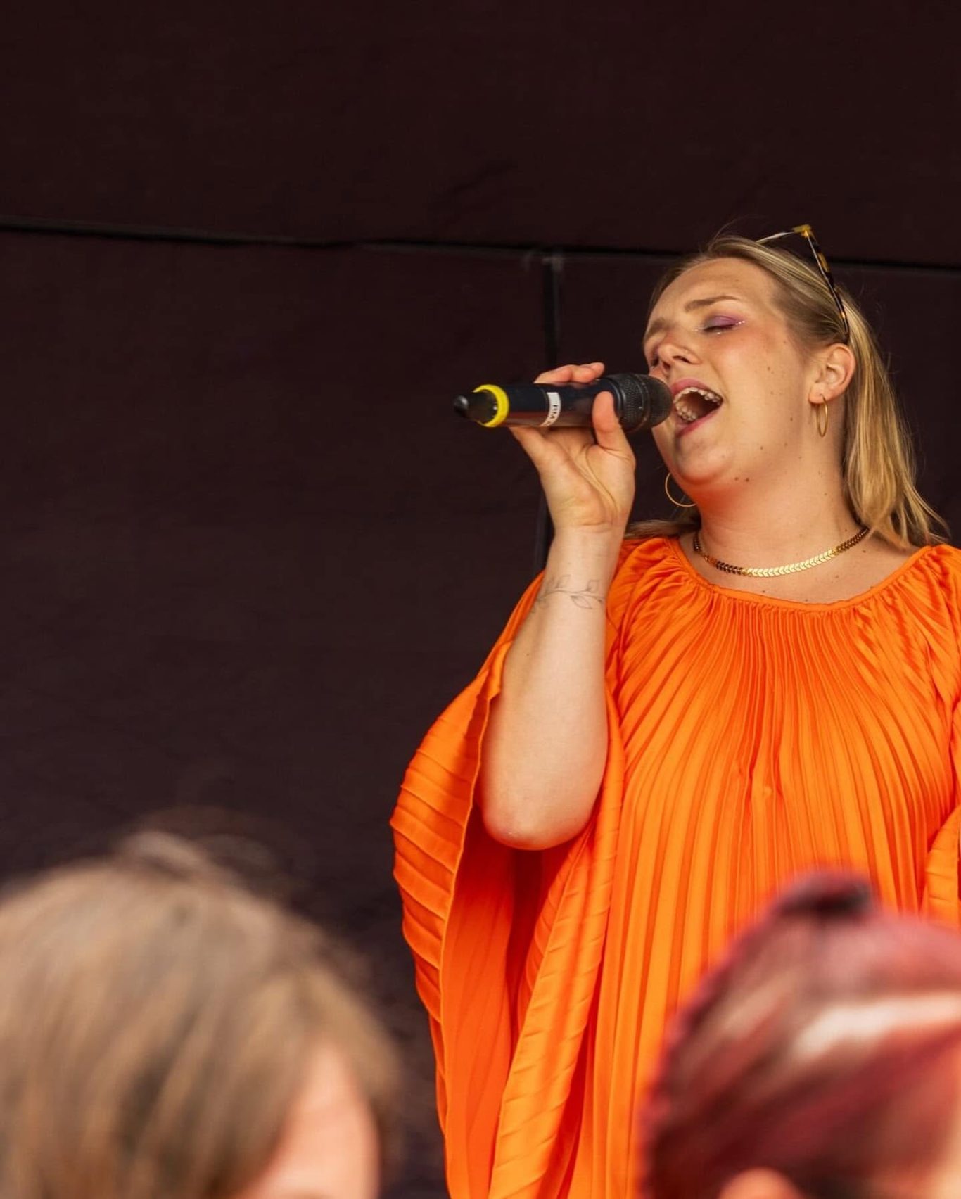 GYG - 2024 Woman in an orange pleated dress singing into a microphone on stage.