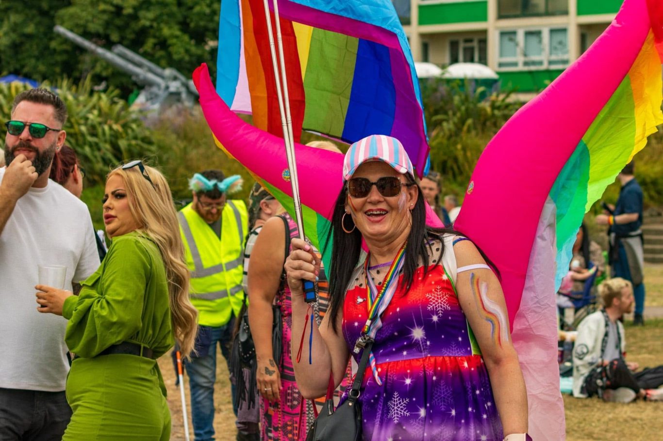 Person in a colourful outfit holds a rainbow flag at a lively outdoor celebration.