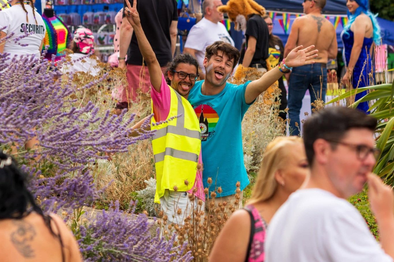 Two smiling people in bright clothing, surrounded by a crowd at an outdoor event.